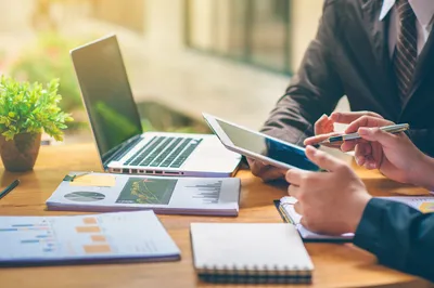 Business professionals reviewing financial charts and documents on a tablet and laptop during a meeting