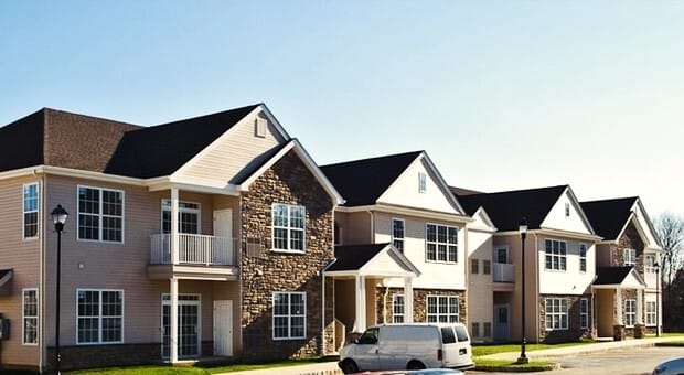 Multi-family residential apartment complex with tan siding, stone veneer, and dark shingle roofs — Englishtown area